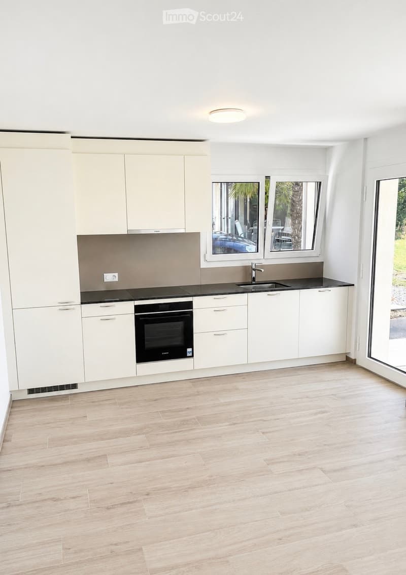 Modern kitchen with white cabinets, black countertops, and a built-in oven. Features a large window with a view of the outdoor area.