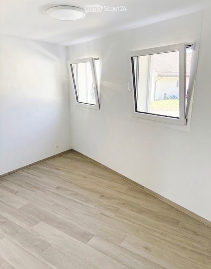 Empty room with light wooden flooring, white walls, and two large windows with white frames.