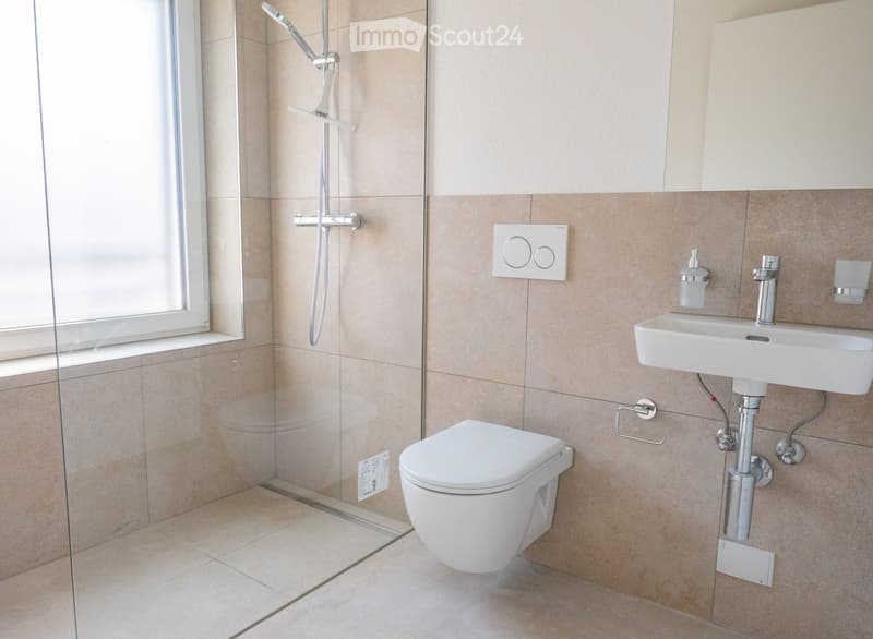 Modern bathroom with beige tiles, a toilet, a sink with a modern faucet, a glass-enclosed shower area, and a towel ring.