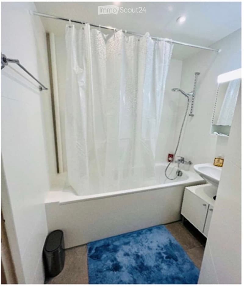 Modern bathroom with a bathtub, shower curtain, sink, cabinet, and a blue rug on the floor.