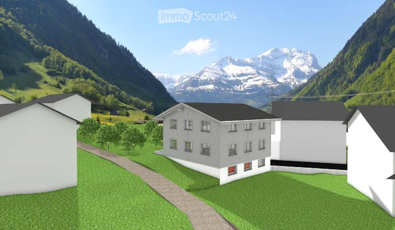 A modern two-story house with white walls and black roof, surrounded by green grass and trees, with snow-capped mountains in the background.