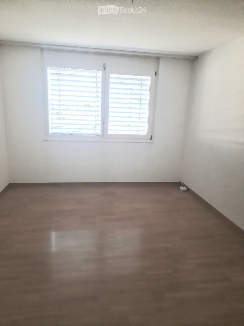 Empty room with bare walls and a polished concrete floor, featuring a single window with blinds.