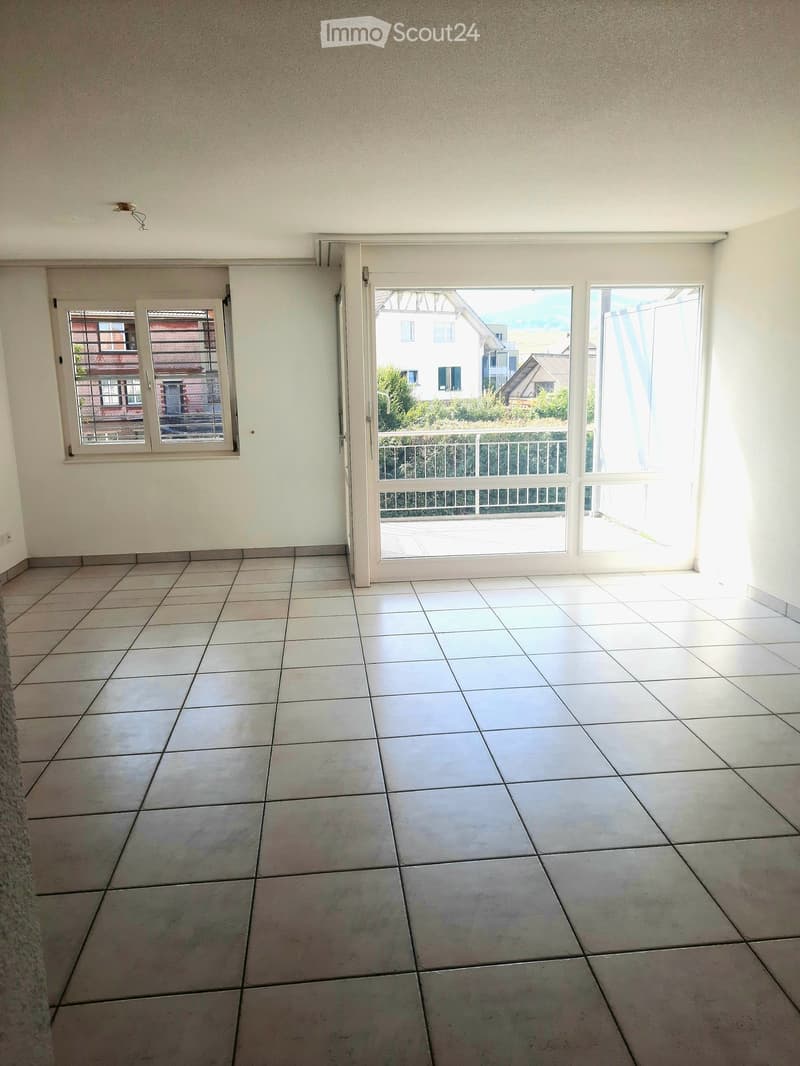 Empty room with tiled floor, white walls, large sliding glass door leading to a balcony, and a window with blinds.