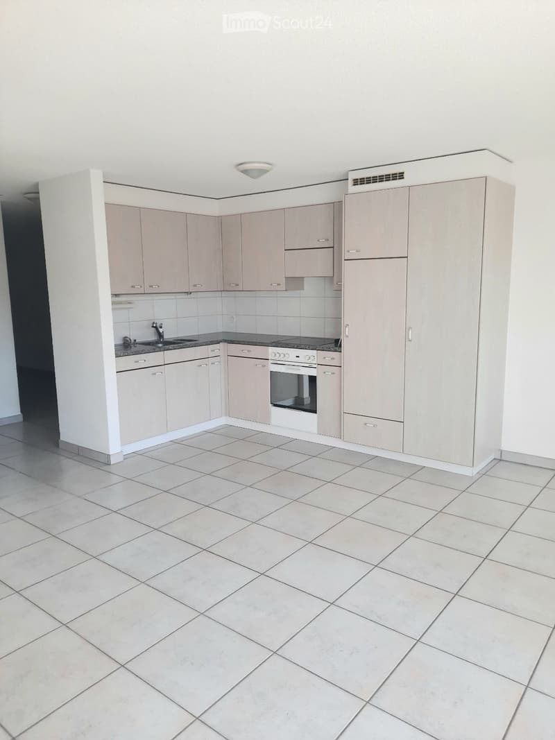 Empty kitchen with light-colored cabinets, a sink, and an oven, featuring tiled flooring and white walls.