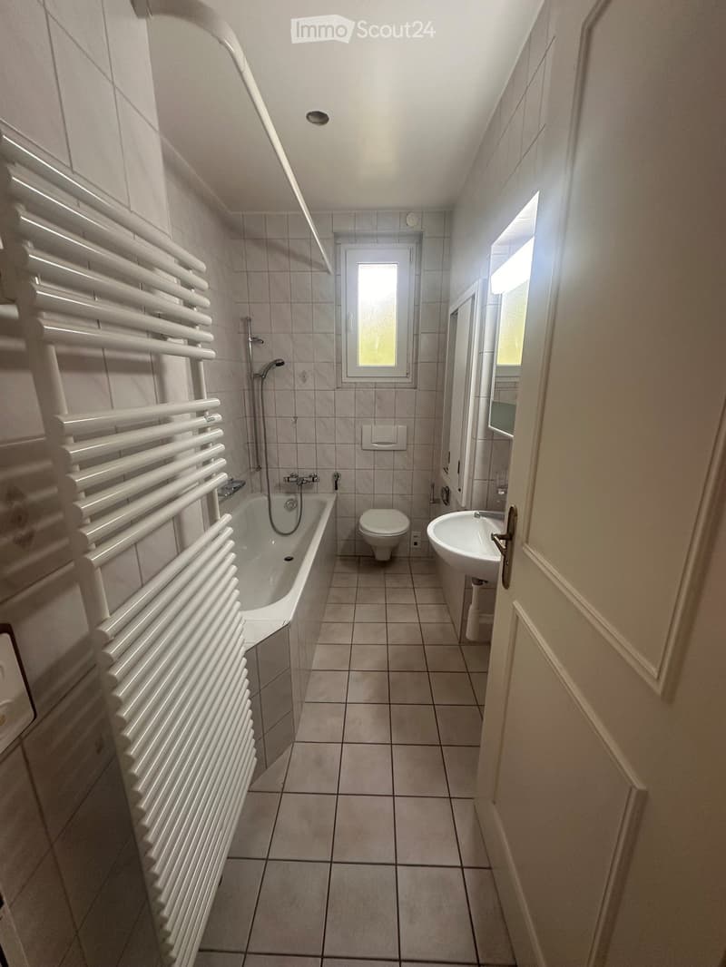 Bathroom with tiled walls and floor, featuring a bathtub, toilet, sink, and a white radiator on the left side.