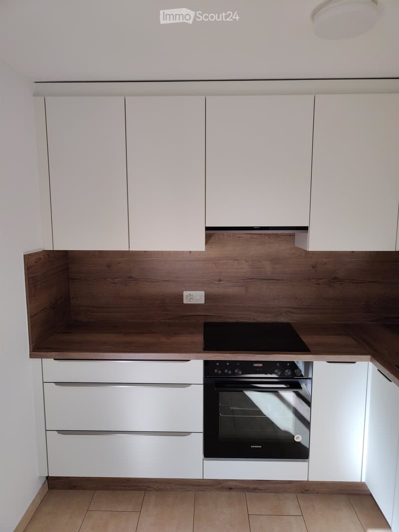 Modern kitchen with white cabinets, wooden countertops, and built-in appliances including an oven and induction stove.