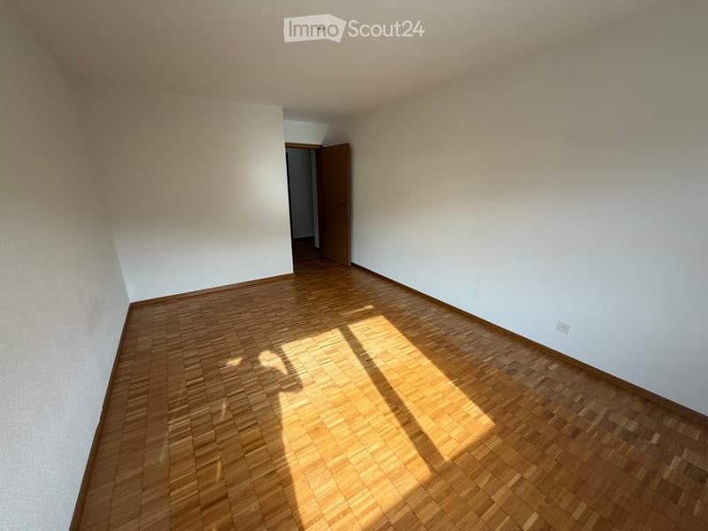 Empty room with wooden flooring and white walls, featuring a doorway leading to another space.