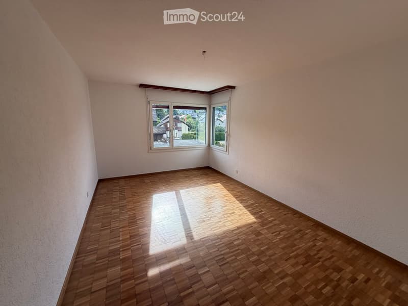 Empty room with wooden flooring and large windows offering a view of the outside. The walls are painted in a light color, and the room has a clean and minimalist design.