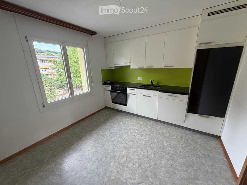Modern kitchen with white cabinets, green backsplash, marble flooring, and large windows offering a view of greenery.