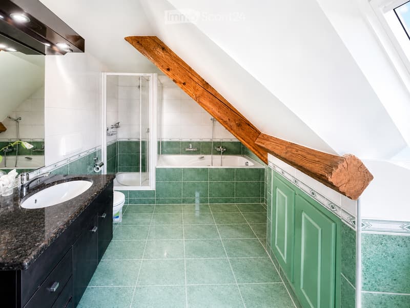 Modern bathroom with green tiles, a wooden countertop, a sink, a bathtub, and a toilet. The room features a skylight and a sleek design.