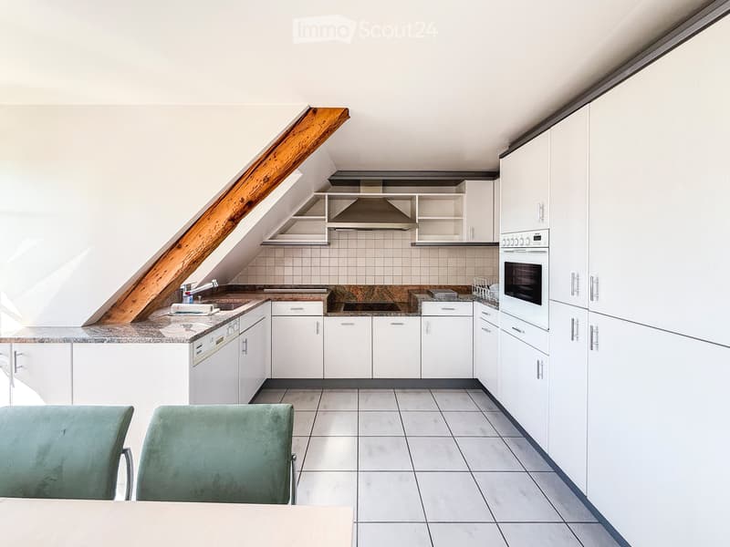Modern kitchen with white cabinets, granite countertops, and built-in appliances, including an oven and a dishwasher. Two green chairs are placed near the counter.