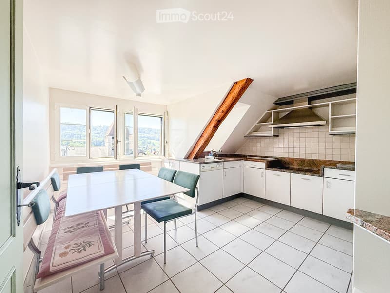 Bright kitchen with white cabinets, a dining table with chairs, and a bench along the wall. The room features large windows offering a scenic view.