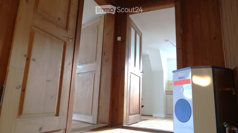 Empty room with wooden walls and doors, leading to another room with white walls and a tiled floor.