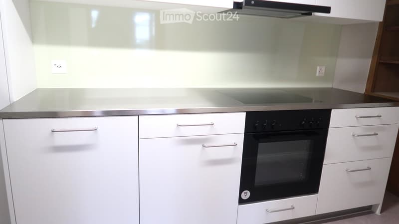Modern kitchen with white cabinets, stainless steel handles, and a built-in oven with a range hood above.