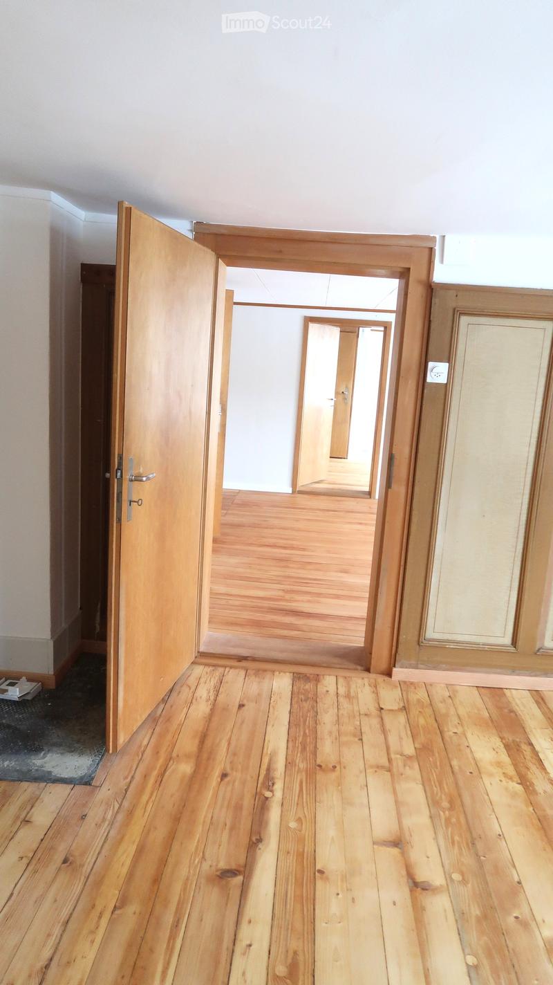 Empty hallway with wooden flooring and white walls, featuring open wooden doors leading to other rooms.