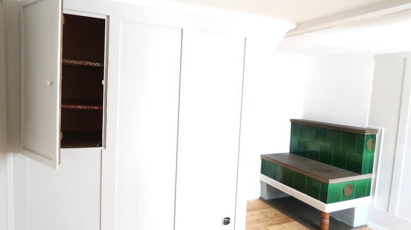 A narrow hallway with white walls, a wooden floor, a green-painted staircase with wooden steps, and an open closet with a colorful interior lining.