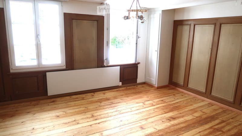 Empty room with wooden flooring, white walls, large windows, and a radiator. No furniture or equipment present.