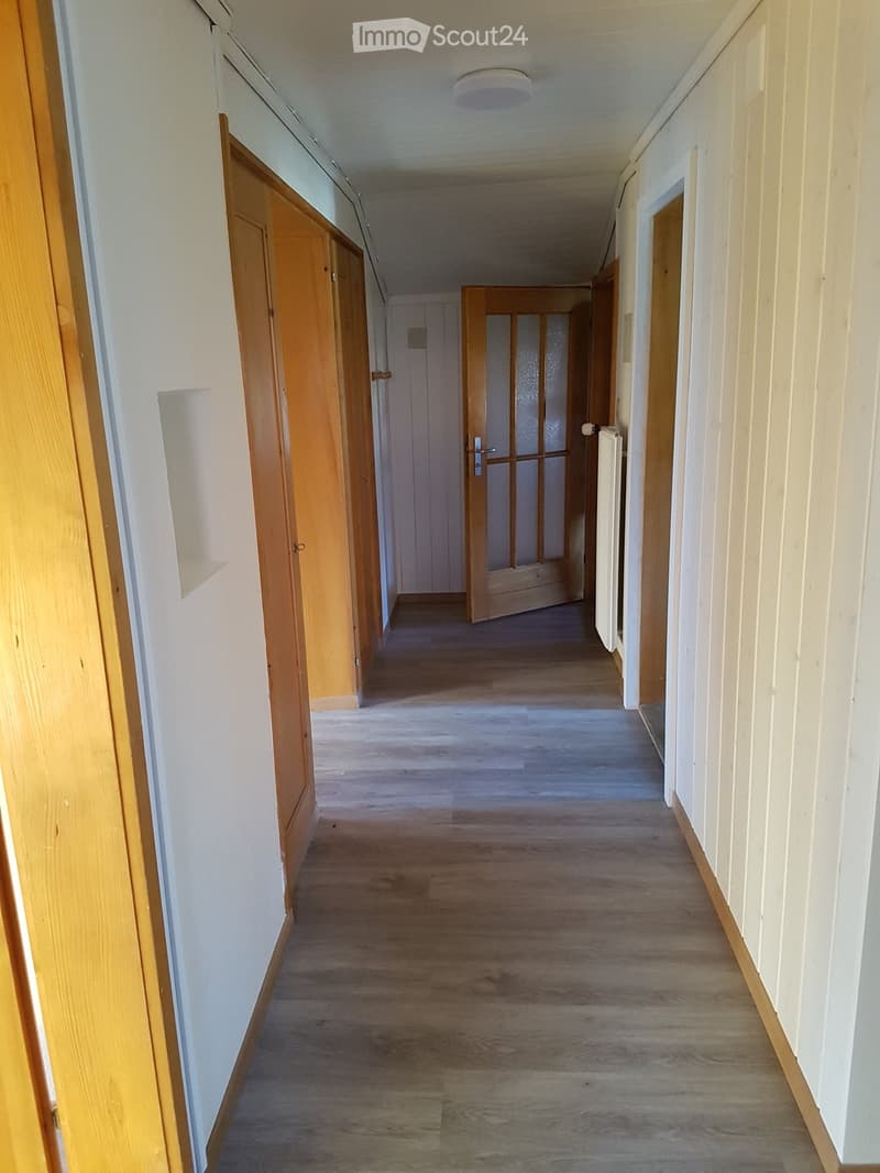 Empty hallway with wooden doors, light-colored walls, and a wooden floor.