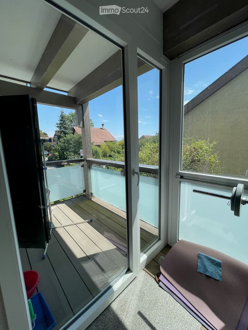 Balcony with wooden decking, glass railing, and outdoor furniture including a lounge chair and small table.