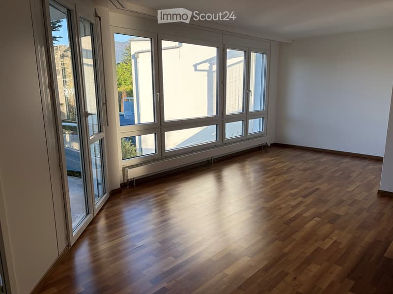 Empty room with wooden flooring and large windows, allowing natural light to fill the space.