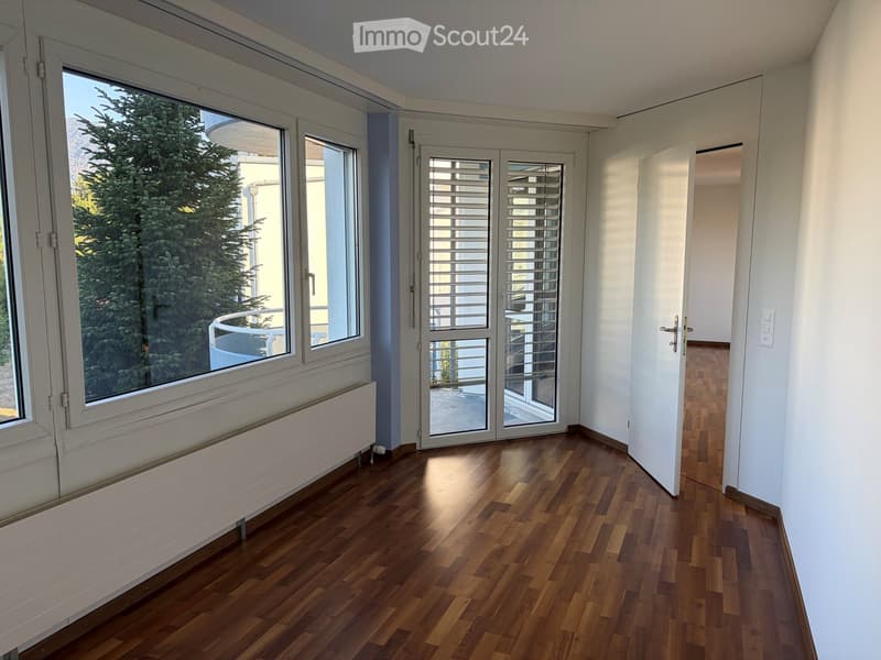 Empty room with wooden flooring, large windows, radiator, and a door leading to a balcony.
