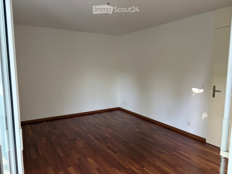 Empty room with wooden flooring and white walls, featuring a door and electrical outlets.