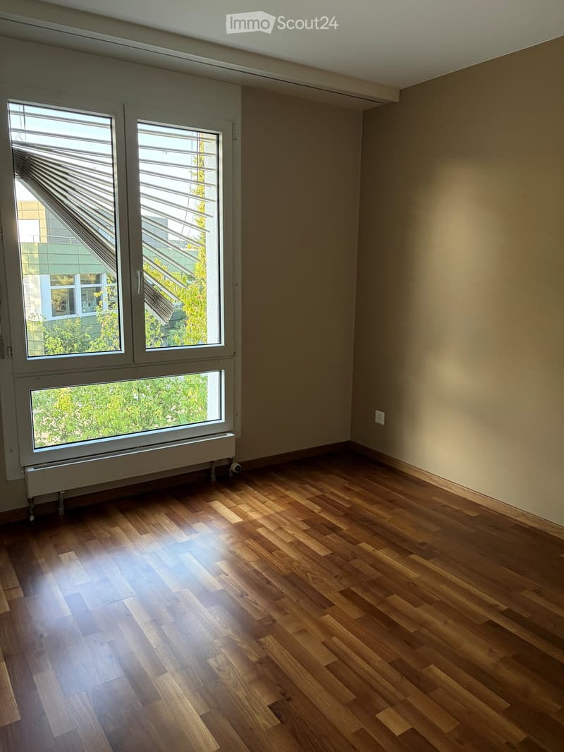 Empty room with wooden flooring, large windows, and neutral-colored walls.
