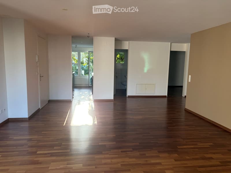 Empty hallway with wooden flooring, white walls, and natural light coming from a window at the end. Doors lead to other rooms, including a bathroom and a room with a bathtub.