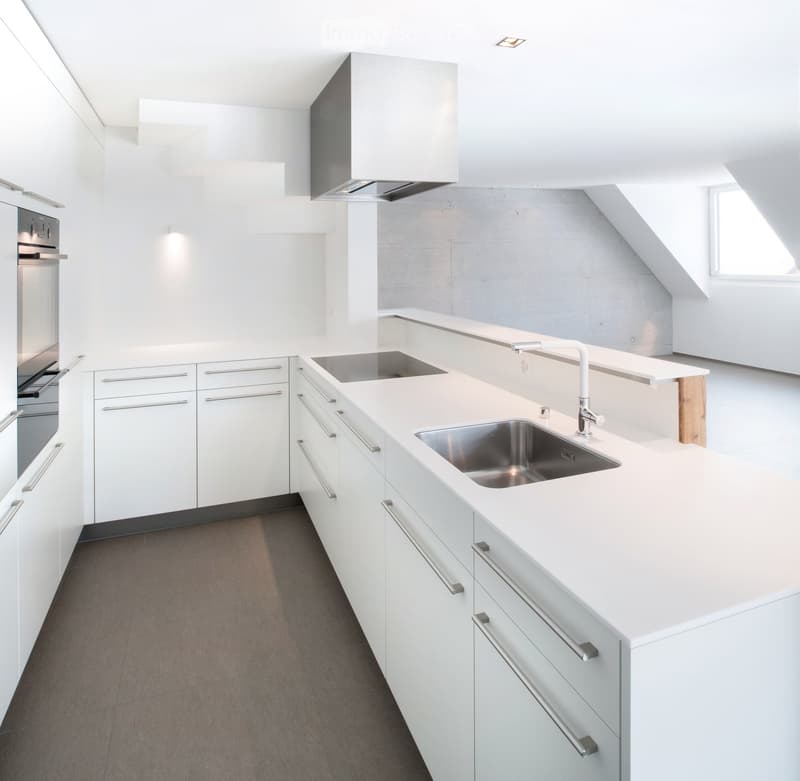 Modern, minimalist kitchen with white cabinets, a central island, a sink, and an oven. The space features sleek, contemporary design elements and ample natural light.