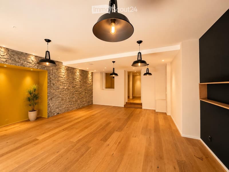 Empty hallway with wooden flooring, stone accent wall, pendant lights, and a potted plant in a yellow accent wall area.
