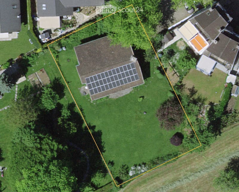 Aerial view of a residential property with a house, solar panels on the roof, and surrounding greenery.