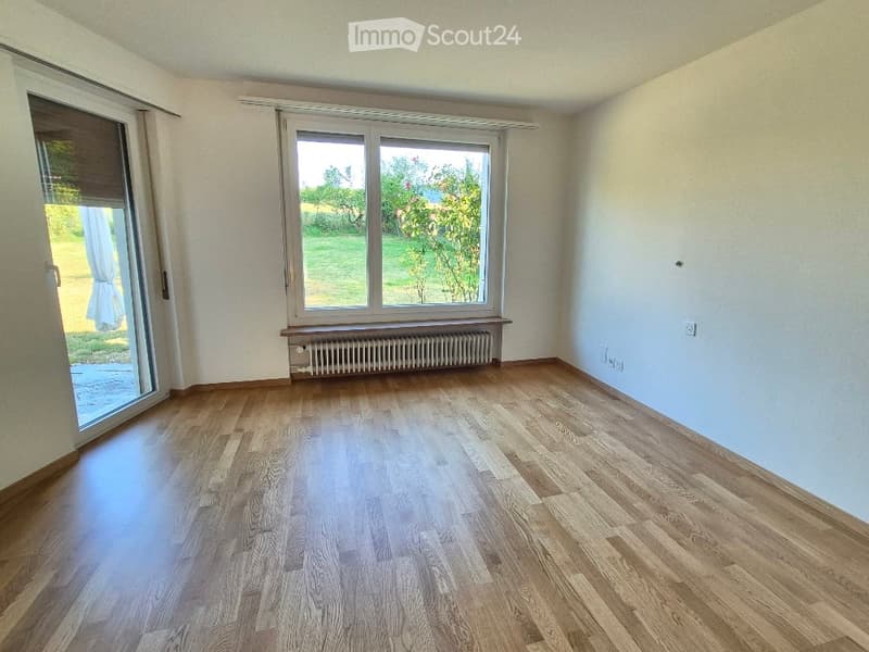 Empty room with wooden flooring, large windows, radiator, and sliding glass door leading to outdoor area.