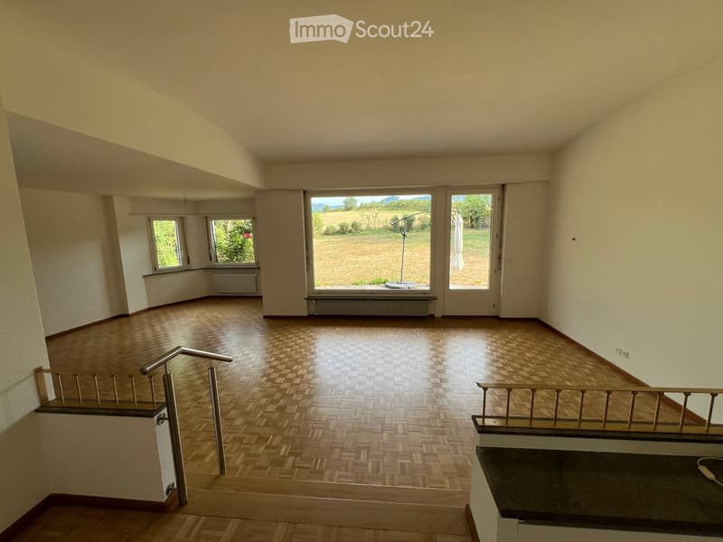 Empty room with wooden parquet flooring, large windows, and a staircase leading to another level.