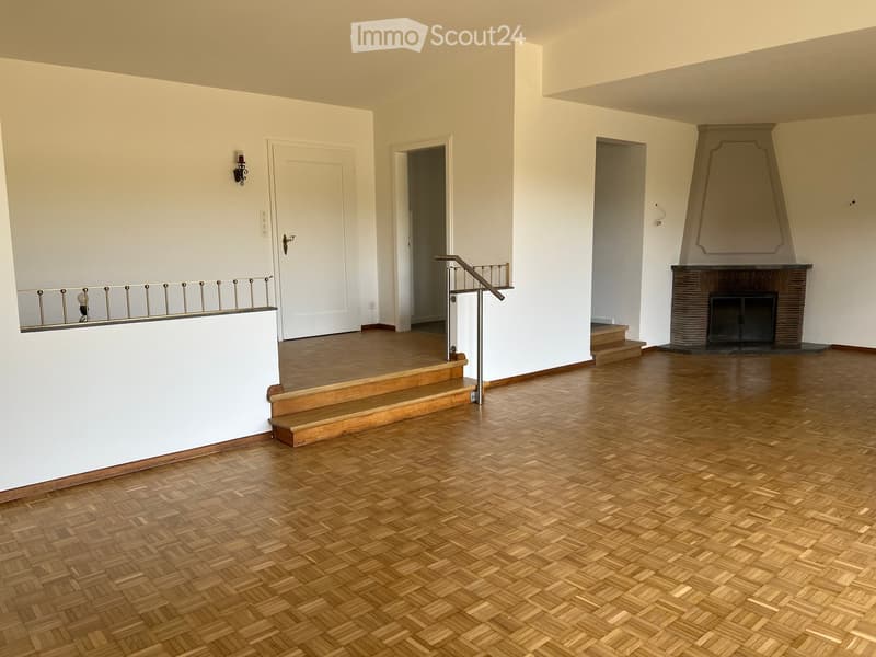 An empty room with wooden flooring, white walls, a staircase leading to another level, and a fireplace with a decorative mantle.
