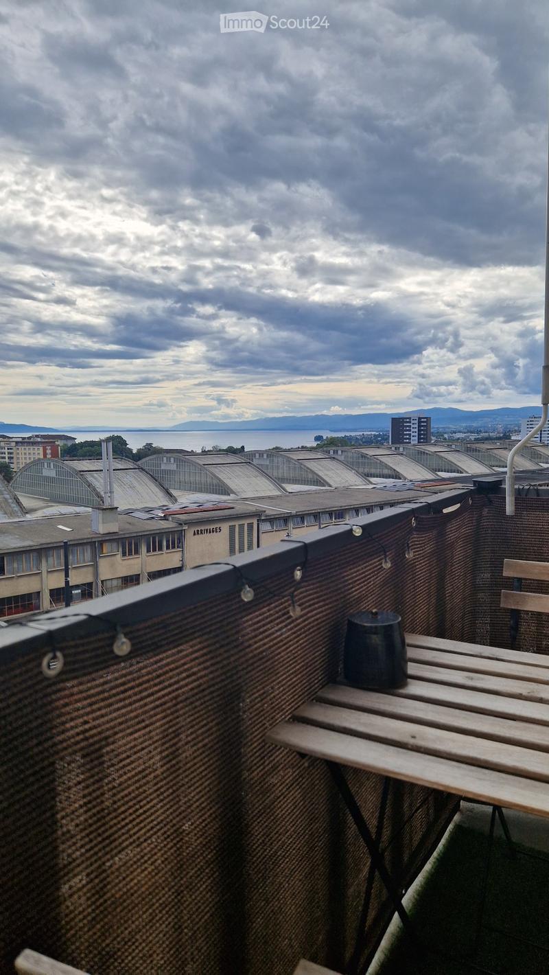 A rooftop terrace with a wooden bench, a small black cup, and a view of the city and distant mountains.