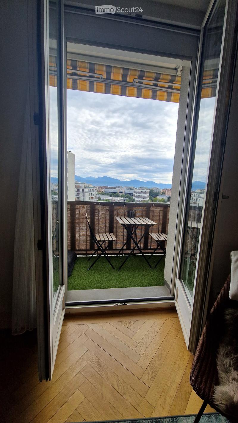 Balcony with a small table and chairs, artificial grass, and a view of the city and mountains.