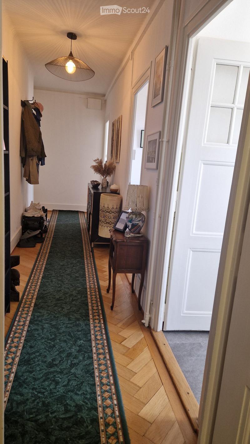 A narrow hallway with wooden flooring, green runner, and decorative items including a lamp, vase, and picture frames.