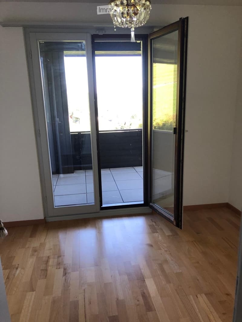 Empty room with wooden flooring and large sliding glass doors leading to a tiled balcony area.