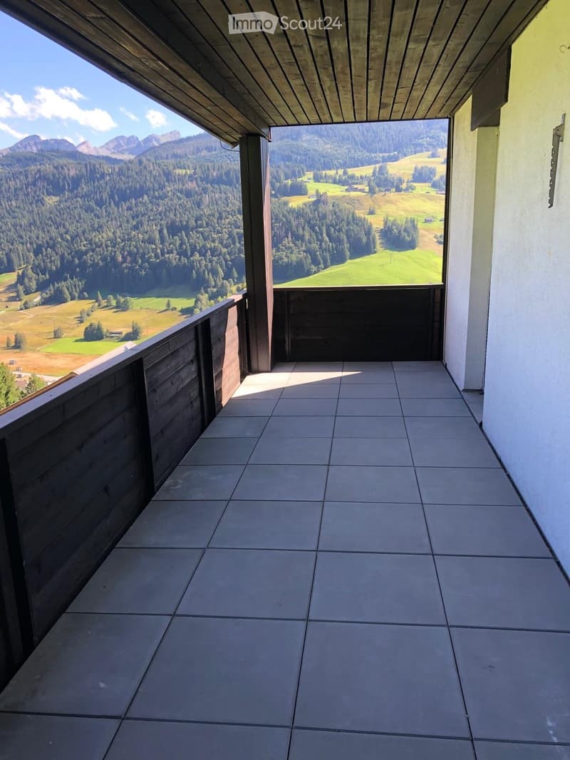 Balcony with tiled floor, wooden railing, and scenic mountain and forest view.