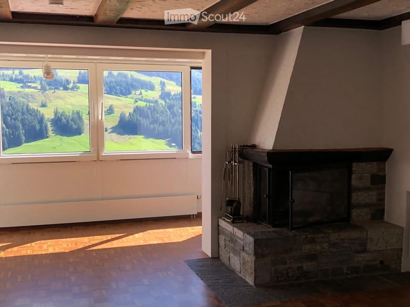 Bright living room with large windows offering a scenic view, featuring a stone fireplace and wooden flooring.