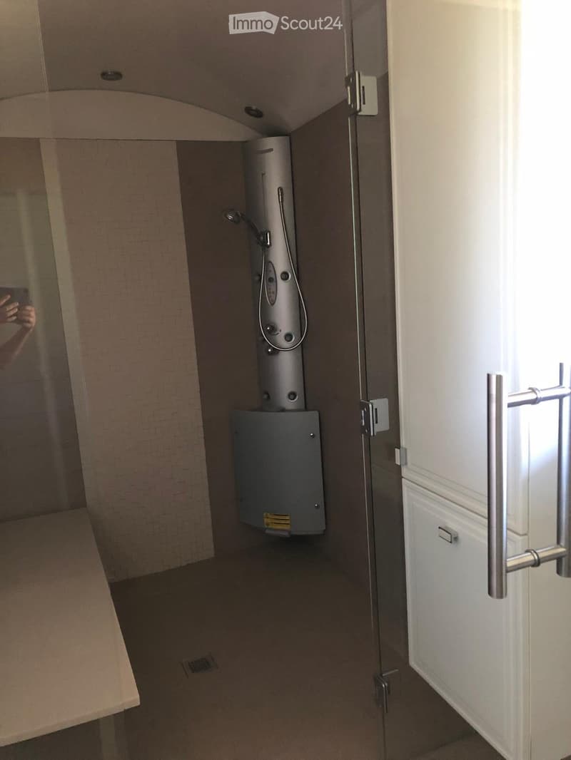 A small bathroom with a modern shower and a water heater unit mounted on the wall. The space features tiled walls and a tiled floor.