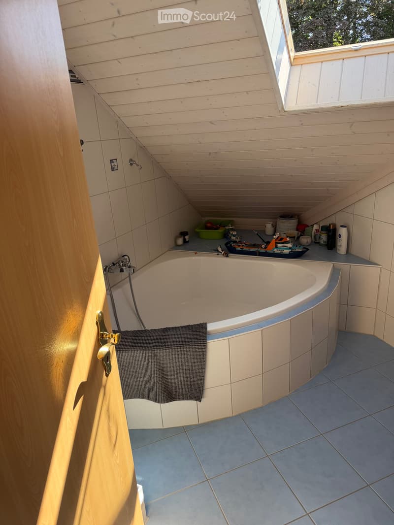 Bathroom with a bathtub, tiled walls, and a window. A towel hangs on the side of the tub, and various items are placed on the windowsill.