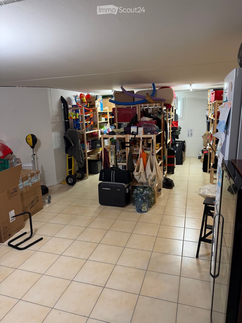 A storage room with tiled floor, shelves filled with various items, a refrigerator, and several bags and boxes scattered around.