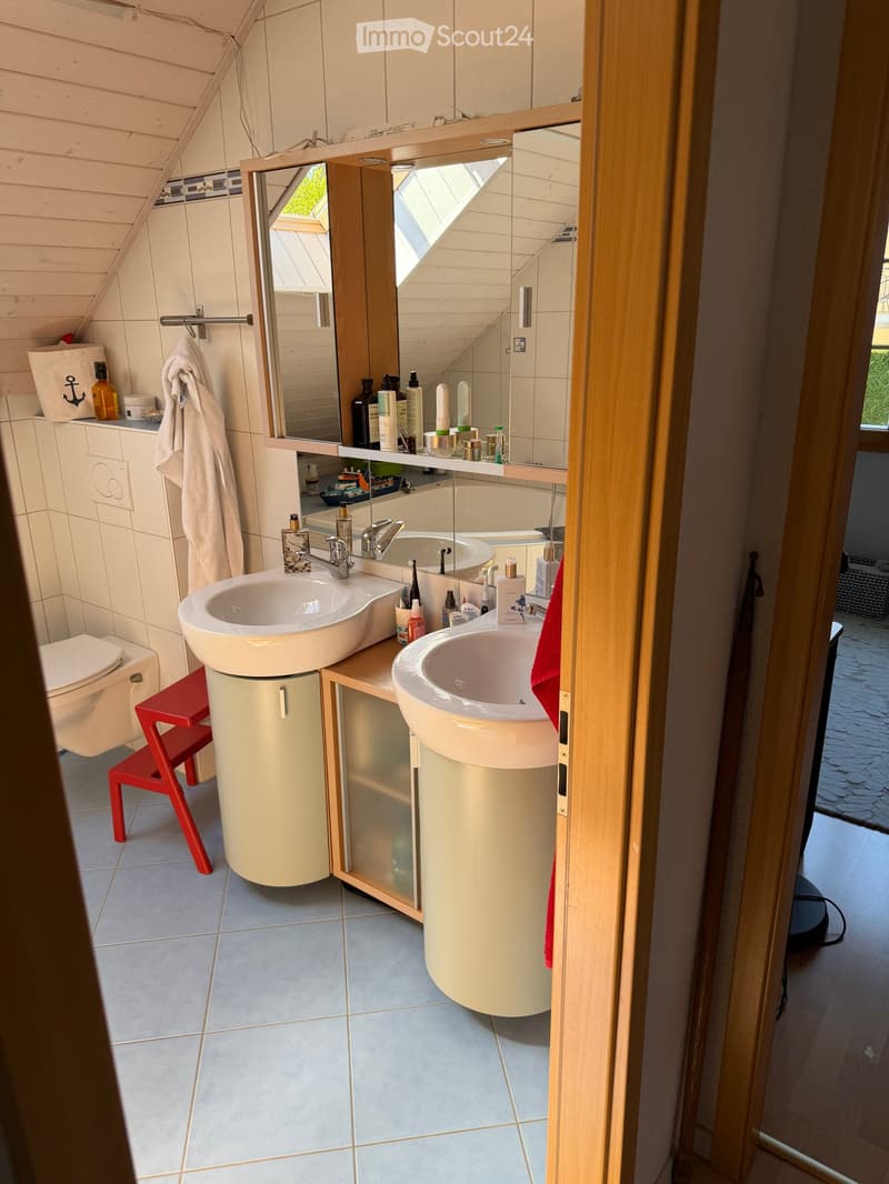Modern bathroom with double sinks, a large mirror, a toilet, a red stool, and various toiletries on the counter.