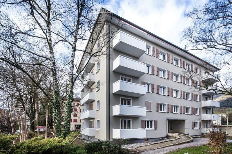 5 story apartment building, white exterior, multiple balconies, set in a park
