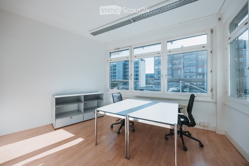 Bright, modern office space with wooden flooring, large windows, a white office table, two office chairs, and a shelving unit.