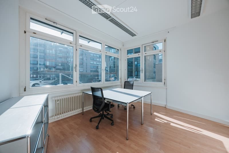 Bright, minimalist room with large windows, wooden flooring, a white table, and a black office chair.
