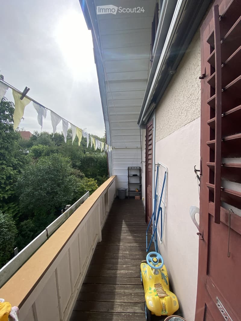 Wooden balcony with railing, small shelf, and a yellow toy car placed on the floor.