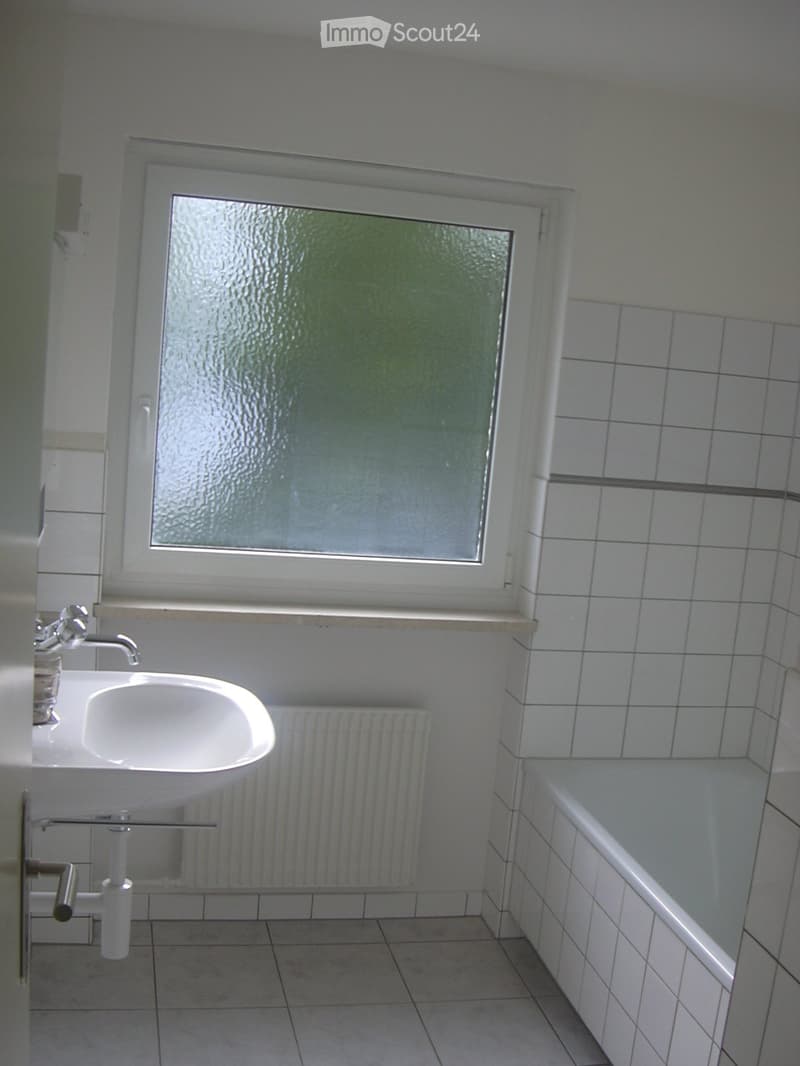 Bathroom with white tiled walls and floor, a white sink with a chrome faucet, and a bathtub. There is a window with frosted glass above the sink.