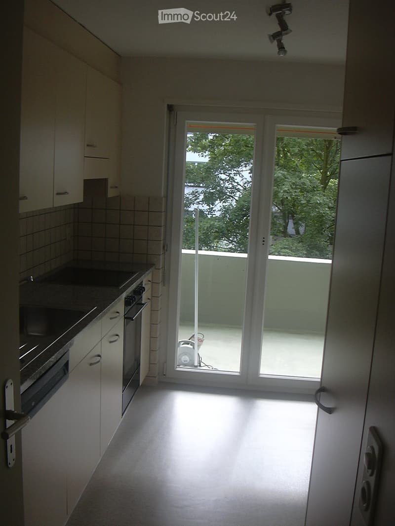 Modern kitchen with white cabinets, a built-in oven, and a large sliding glass door leading to a balcony or outdoor area.